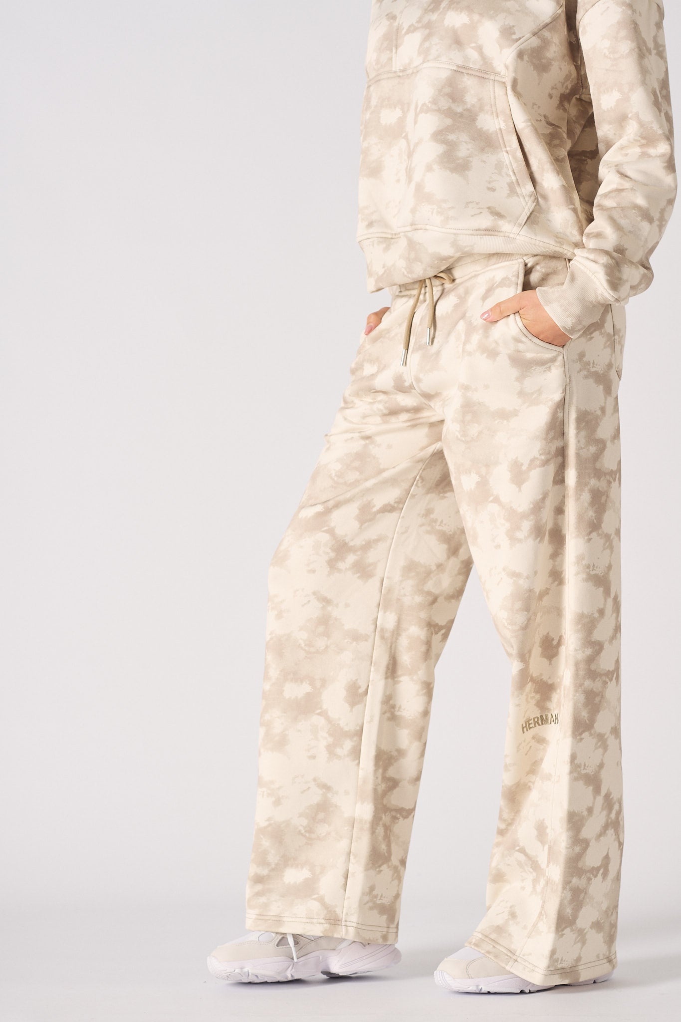 Model posing in a relaxed stance wearing beige tie dye wide leg joggers
