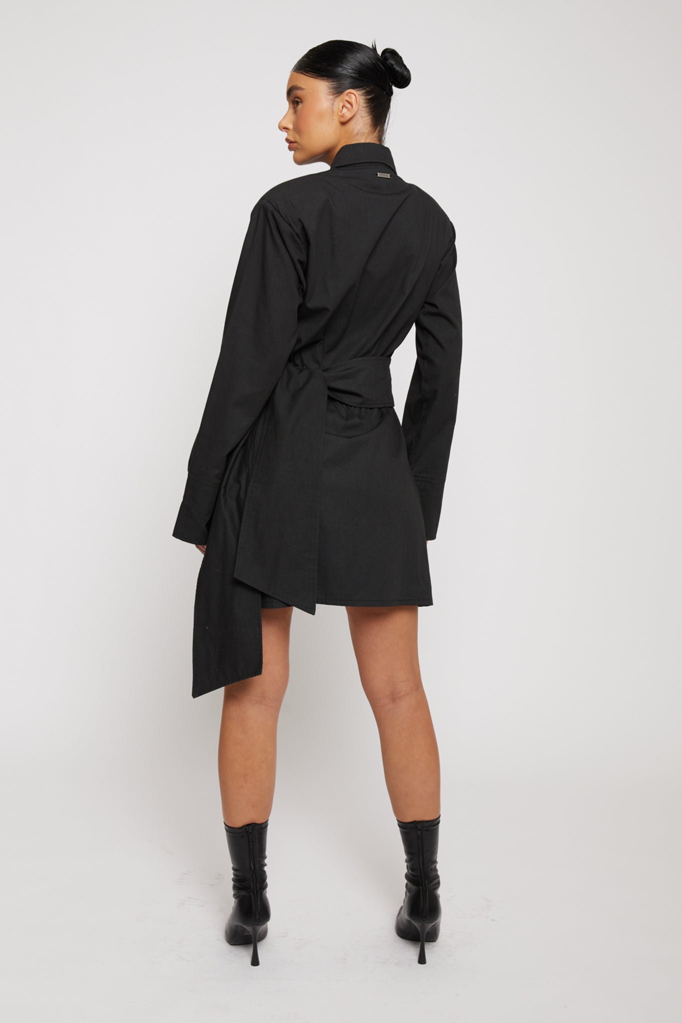 Back view of a model in the black cotton asymmetric shirt dress.