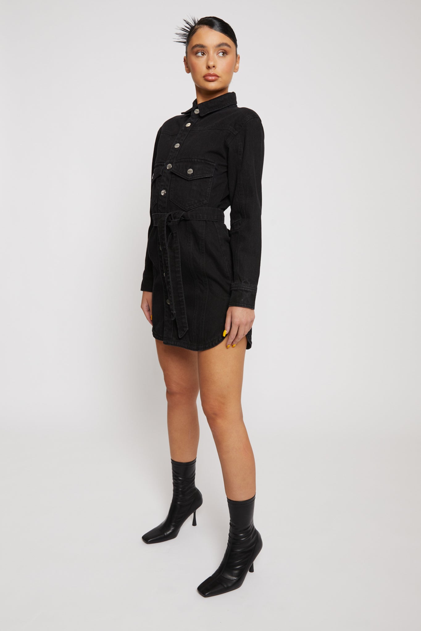 Side angle of a model wearing the black jean dress with a belt, showing the fit