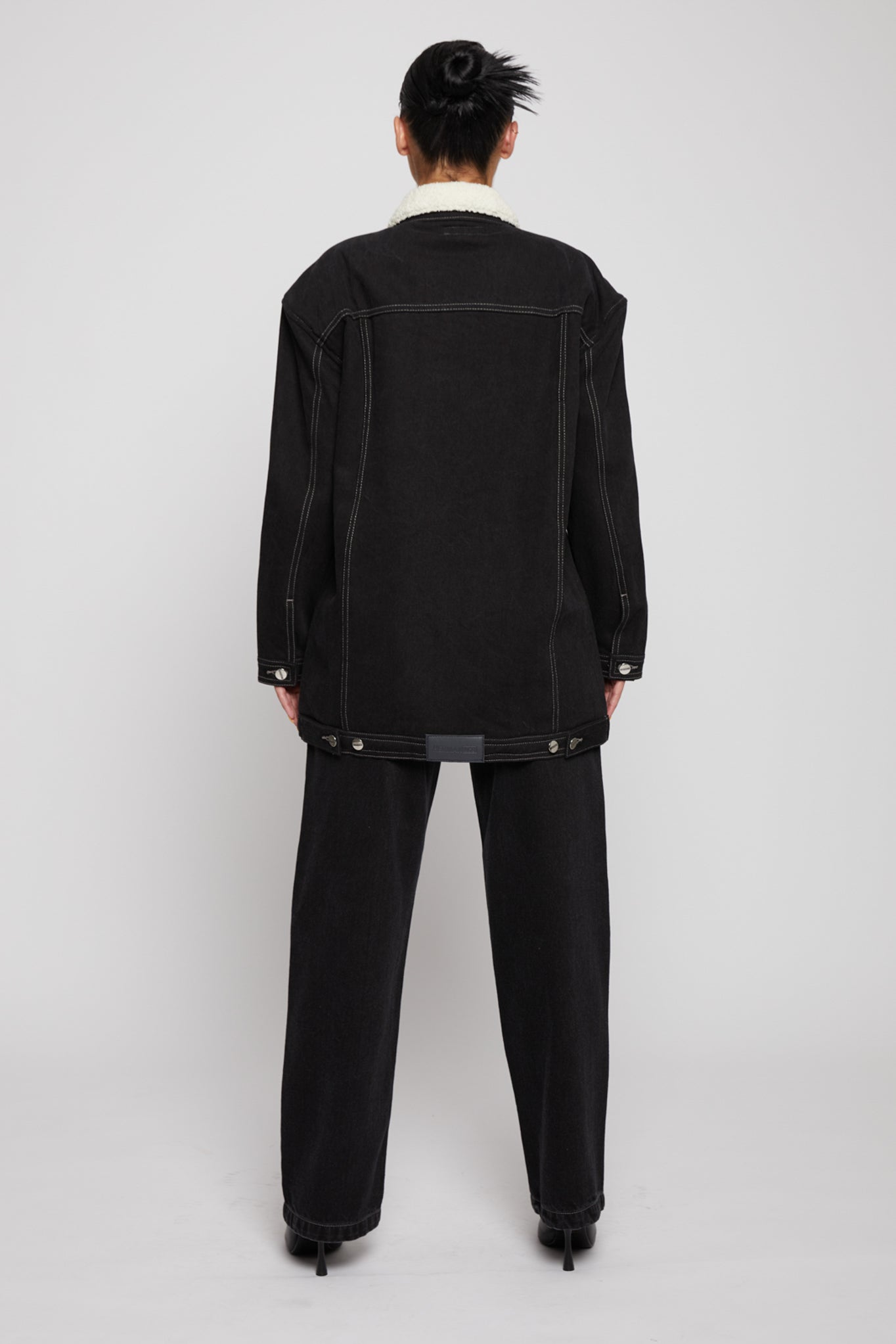 Back view of a model wearing the black shearling jean jacket.