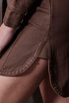 Detailed view of the curved hem and side slit on the brown denim shirt dress
