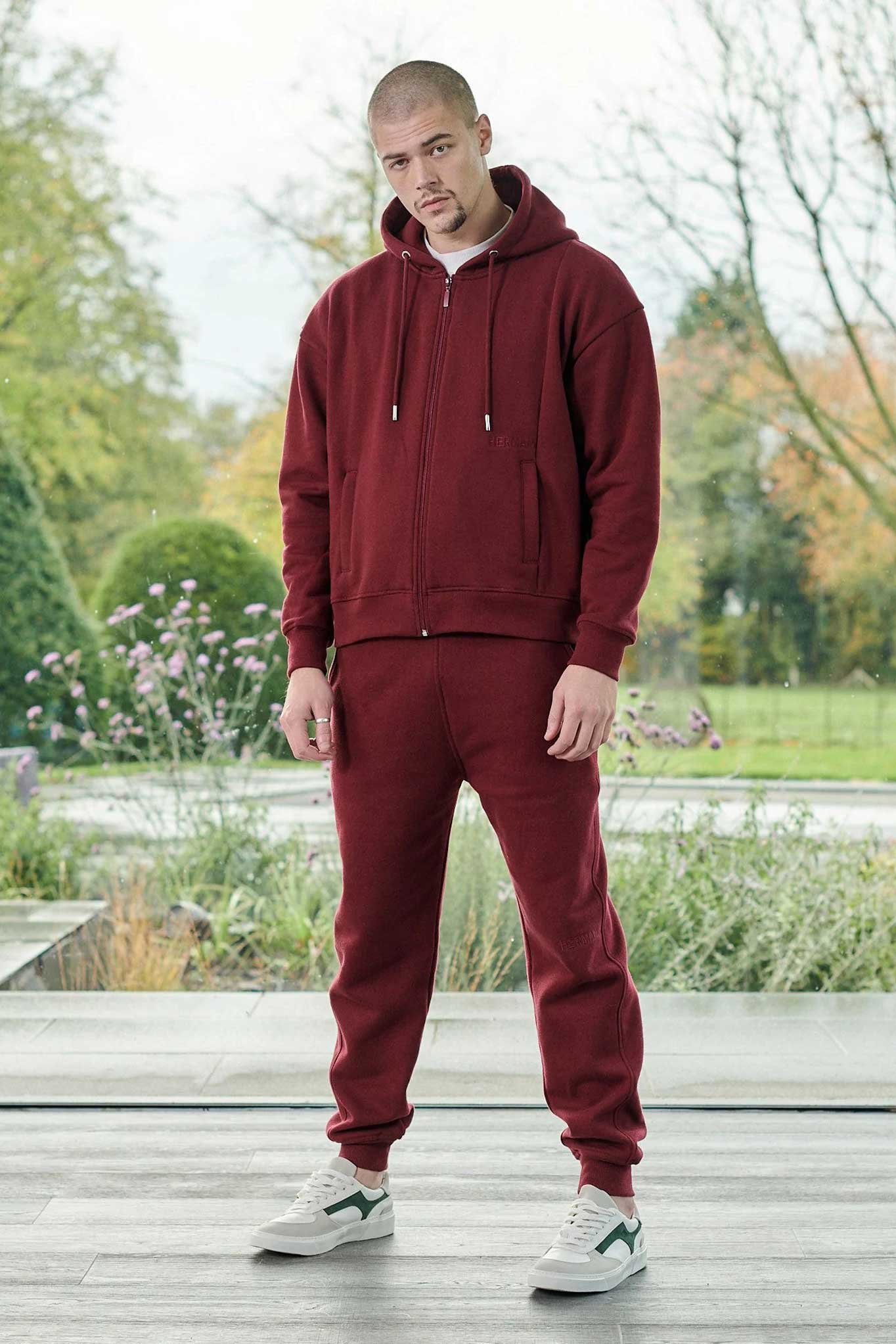 A model wearing the dark red tapered joggers for men with a matching zip hoodie.