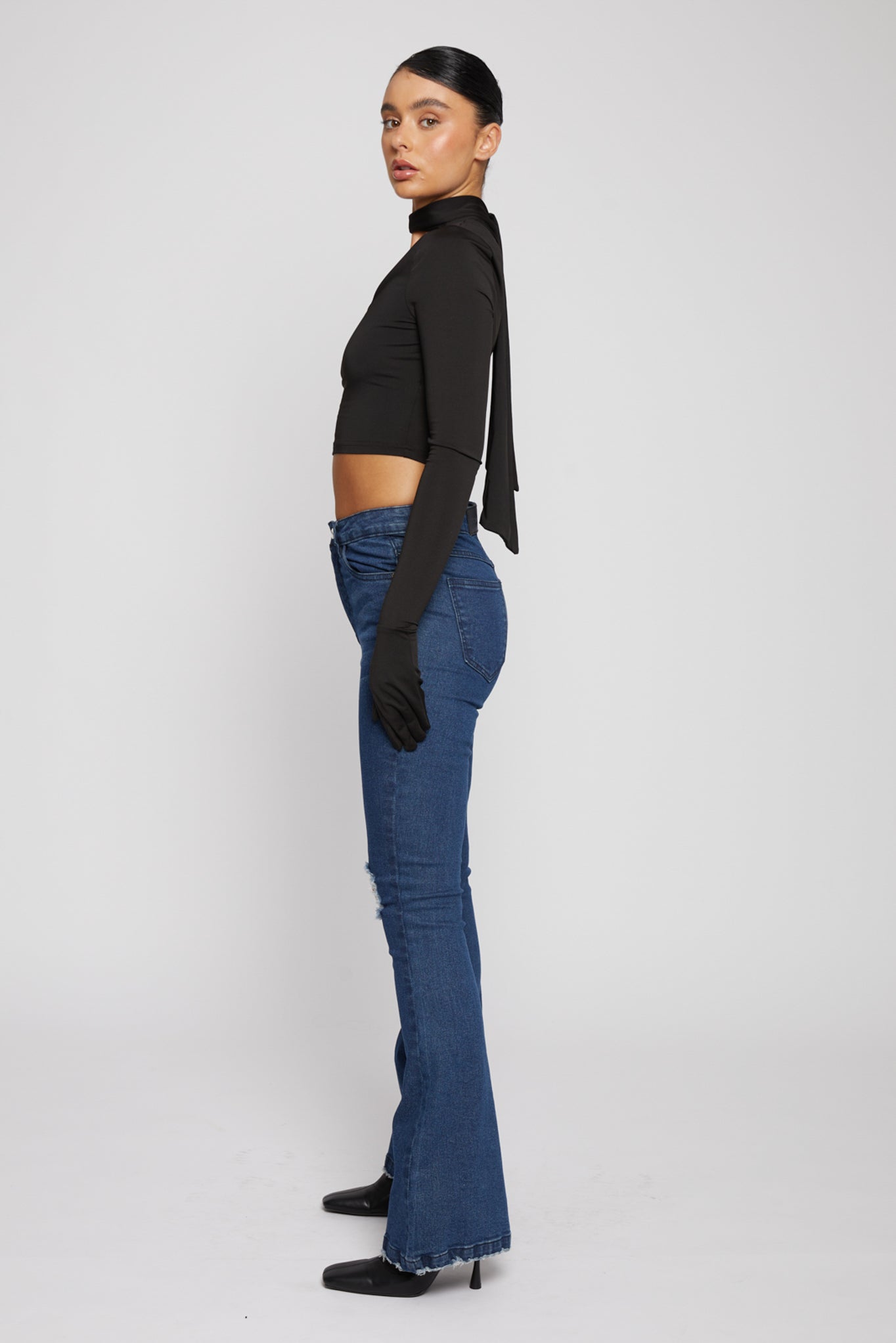 Side profile of a model showing the fit of the dark wash distressed flare jeans.