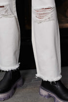 Close-up of the frayed hem and distressed knee detail on the off-white jeans.
