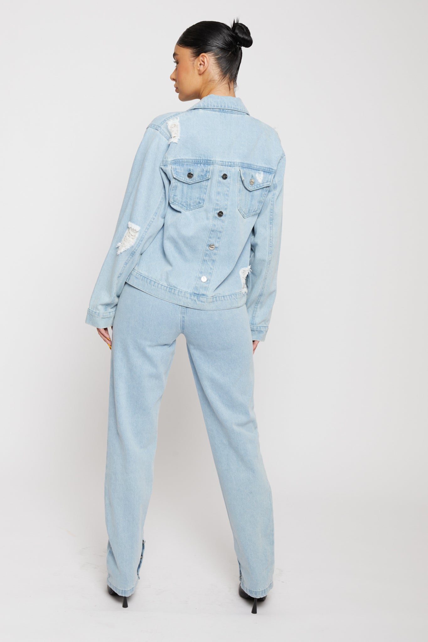 Back view of a model in the distressed light wash denim jacket showing button details.