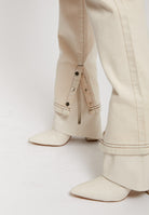 Detailed view of the popper and zip detail on the hem of the ecru jeans