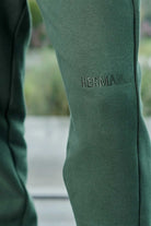 Close up detail of HERMAN text embroidery on the leg of green joggers