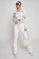 A model styled in high-waisted white flare jeans with a printed top and handbag.