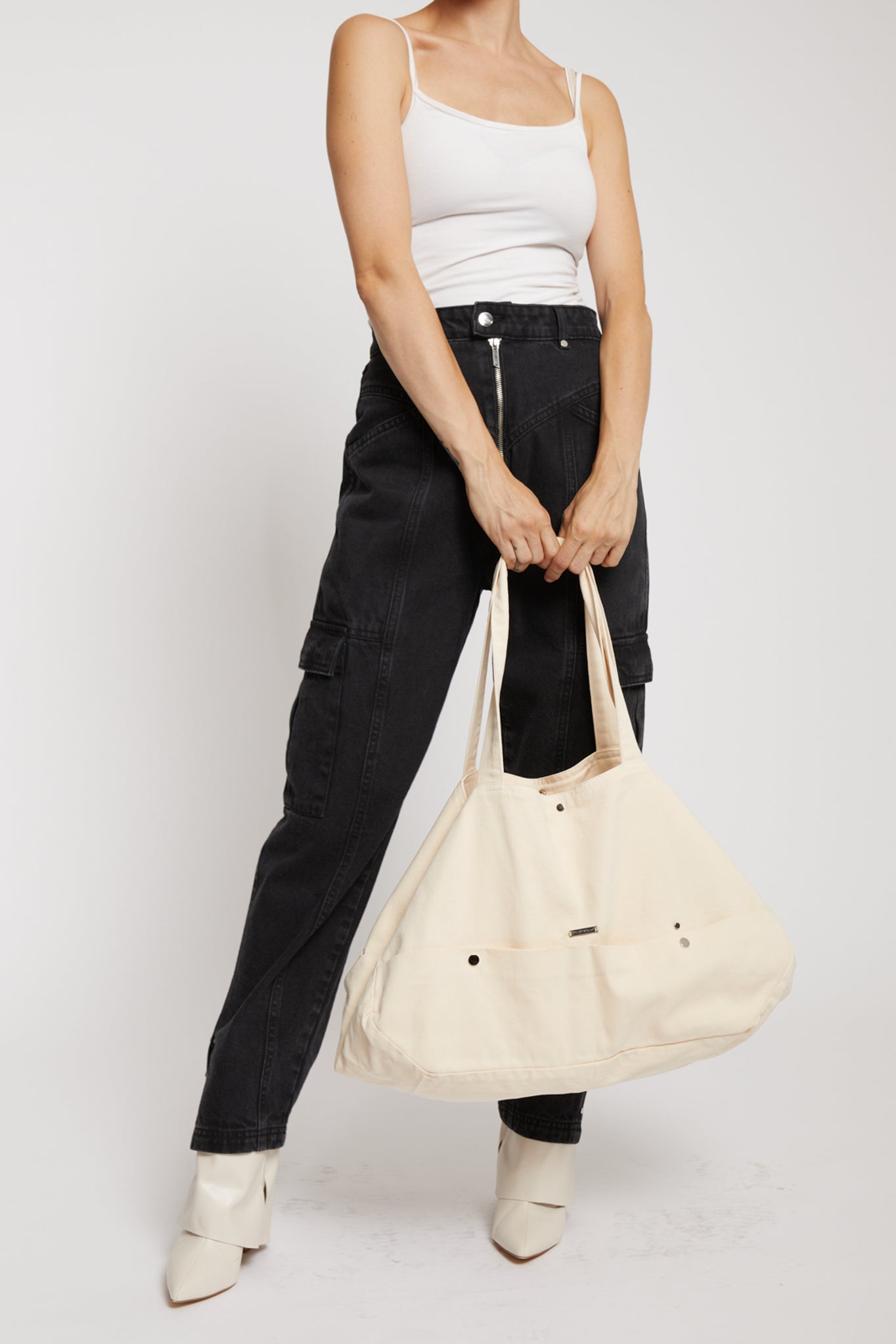 A model holding the large ecru tote bag with black cargo pants