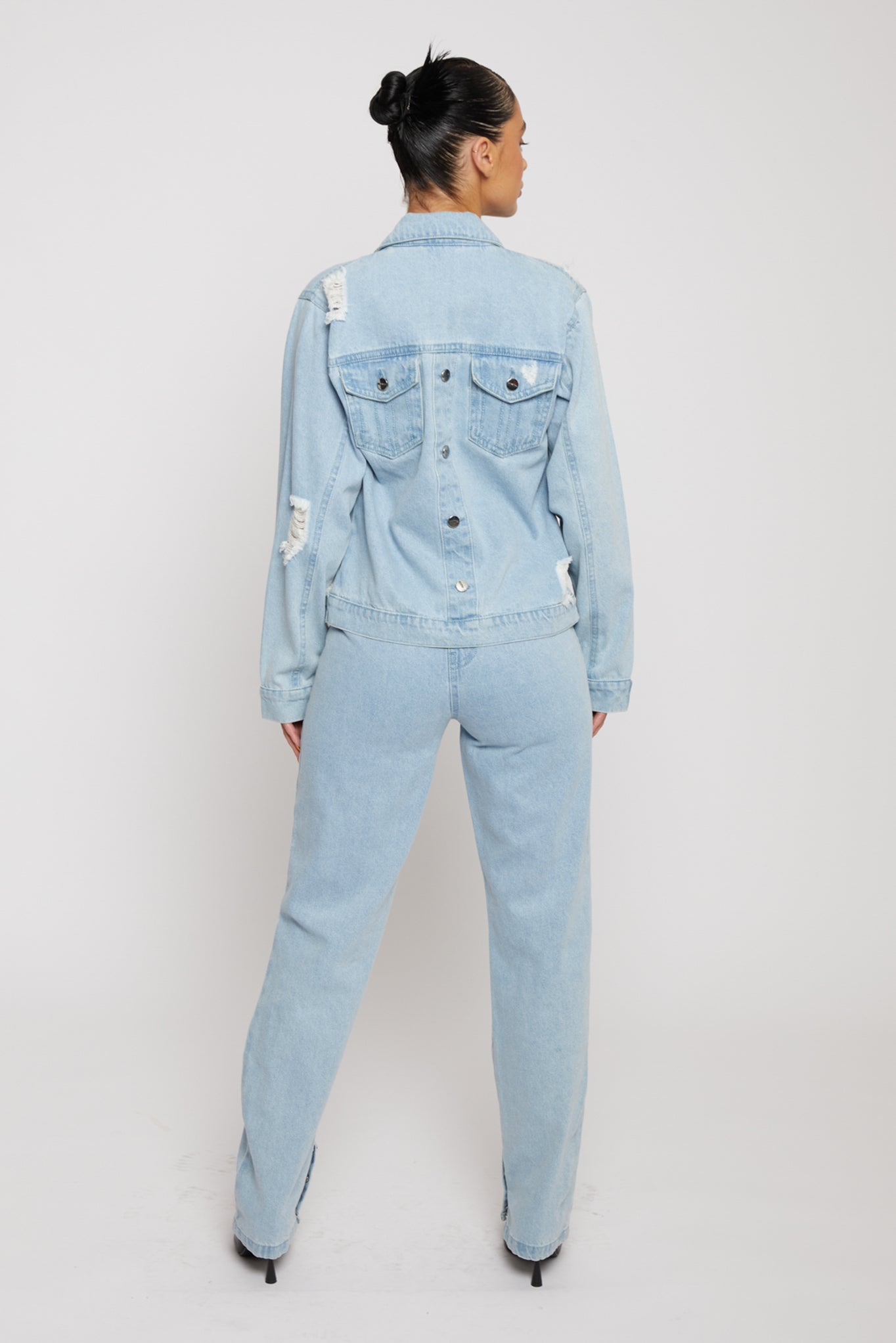 Full back view of a model in the light wash denim jacket and jeans set.