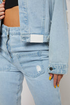 Detailed view of the white logo patch on the light wash denim jacket.