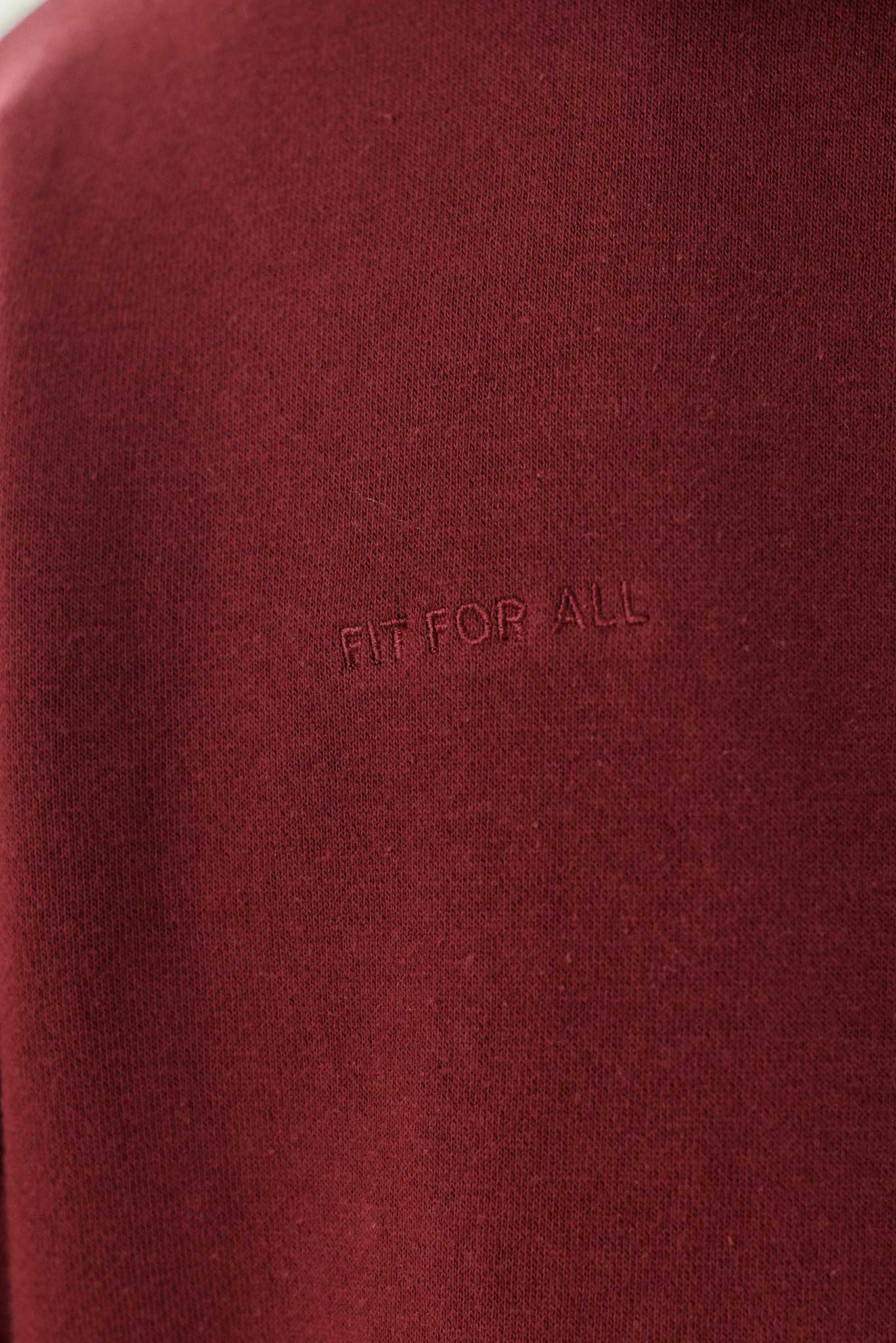 Close-up of the tonal 'Fit For All' embroidery on the maroon zip-up hoodie