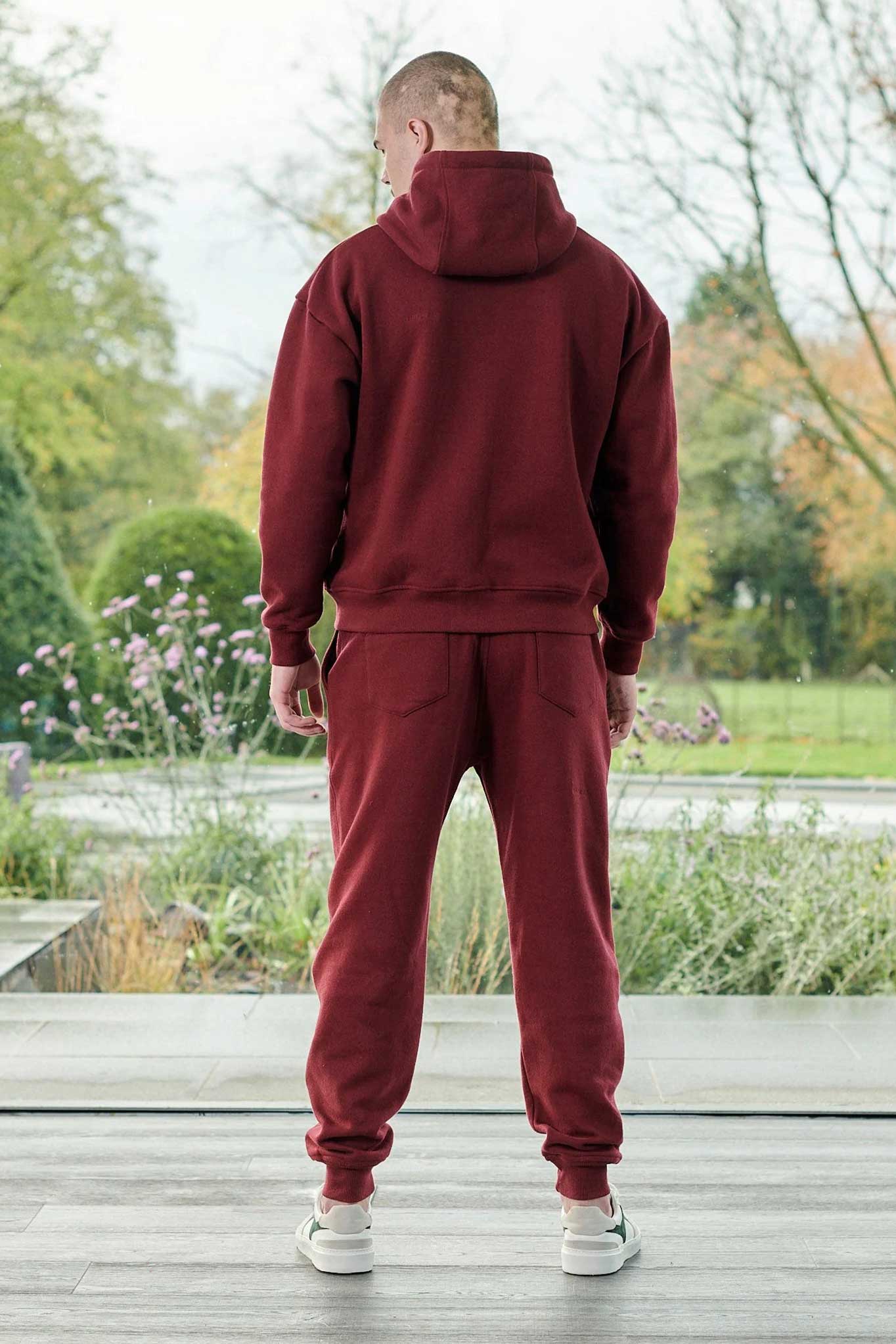 Back view of a model in the men's dark red jogger and matching hoodie set.