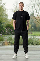 A model wearing men's black tapered joggers with a matching t-shirt