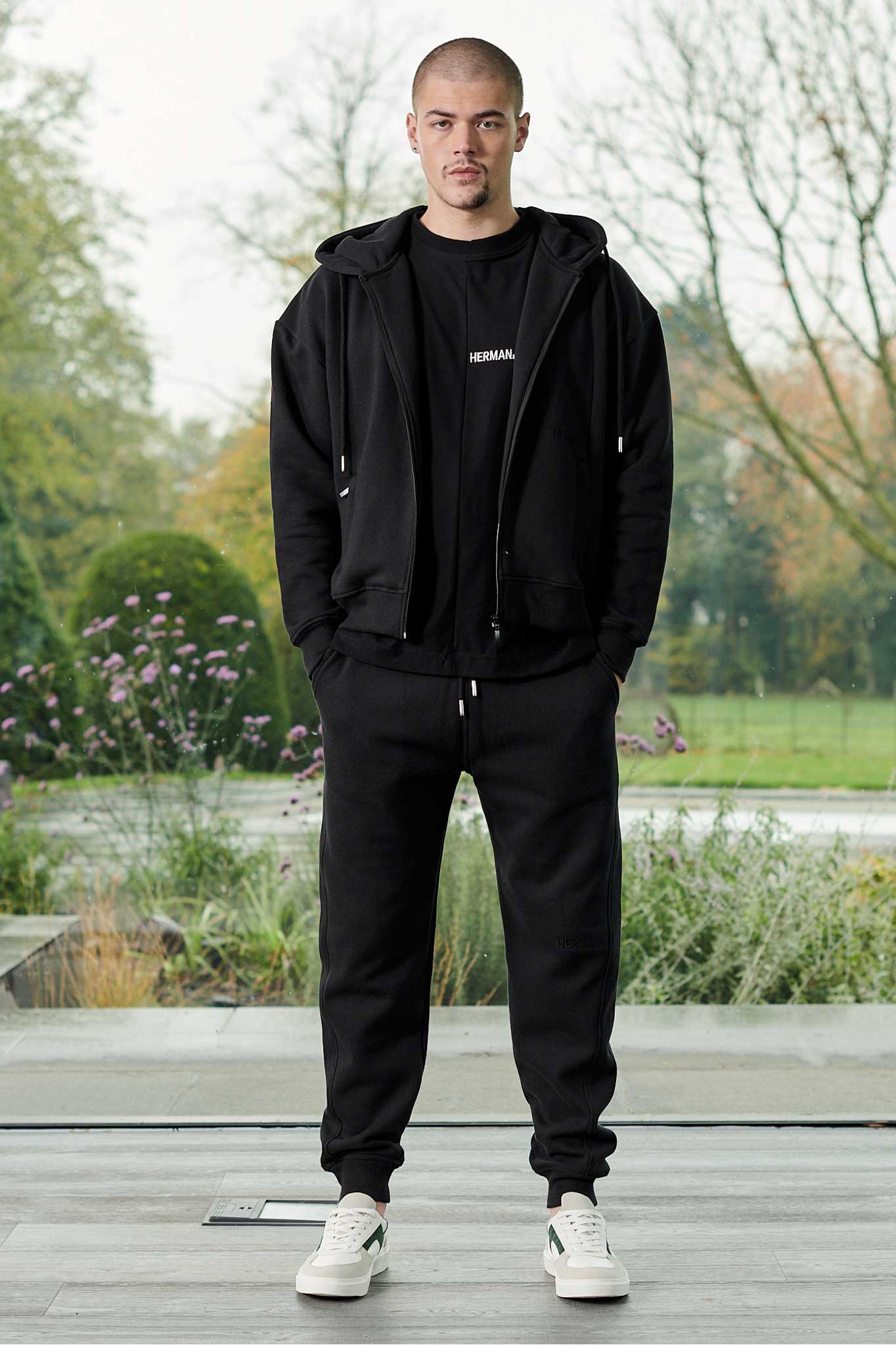 Front view of model wearing mens black zip up hoodie with matching joggers