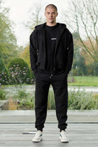 Front view of model wearing mens black zip up hoodie with matching joggers