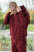 A model adjusting the hood of the men's maroon zip-up hoodie.