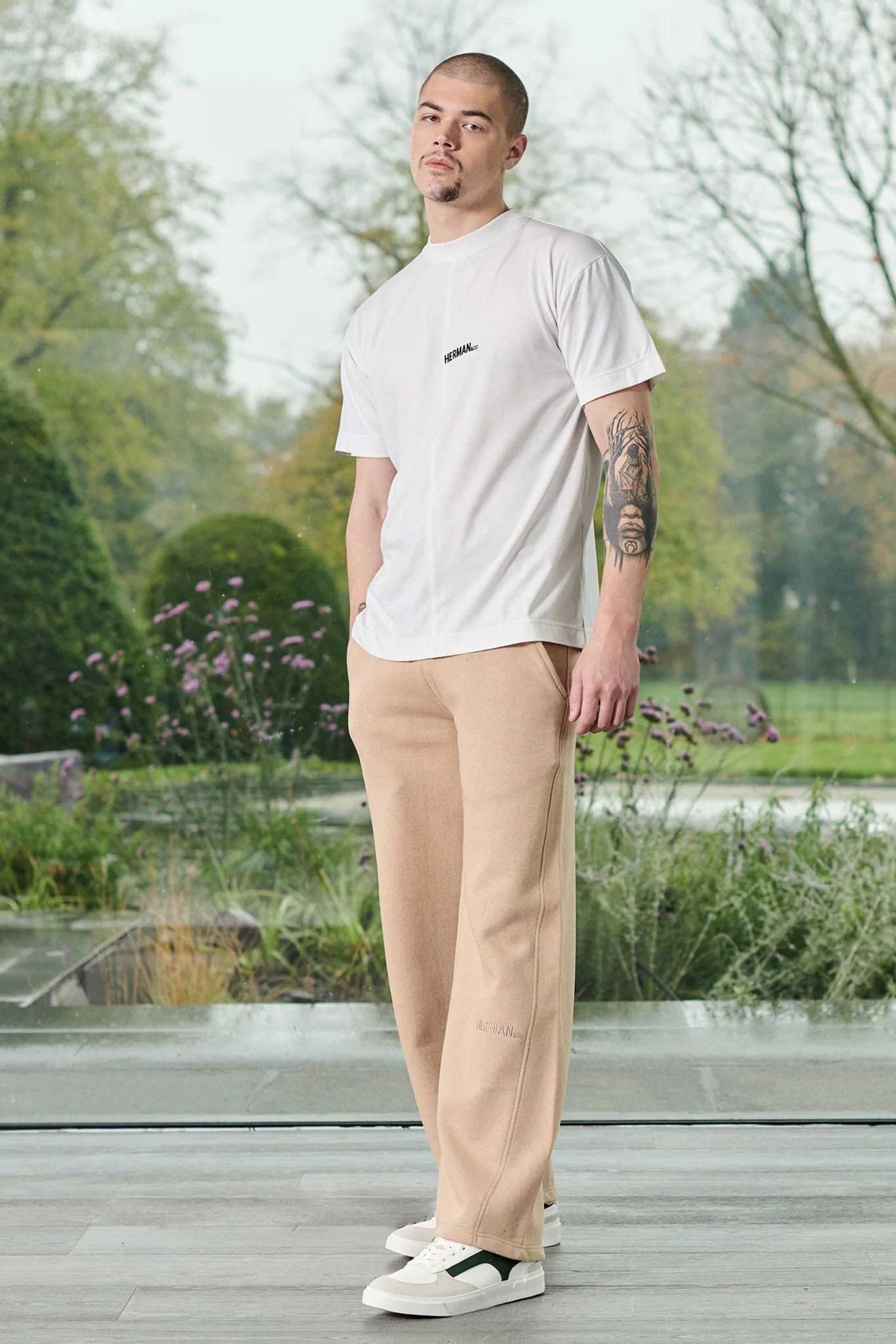 A man wearing an oversized white t-shirt outfit with beige trousers.