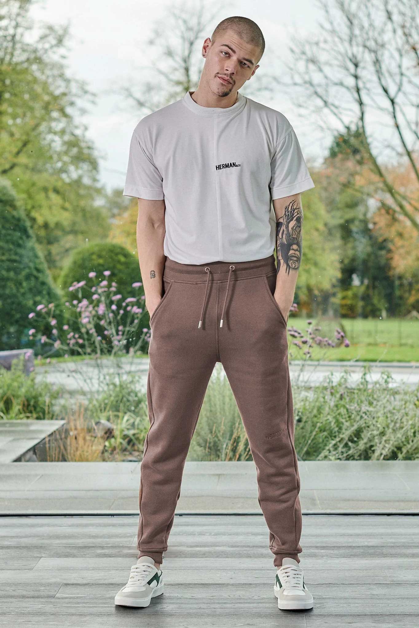 A model styled in the men's brown tapered joggers with a white t-shirt