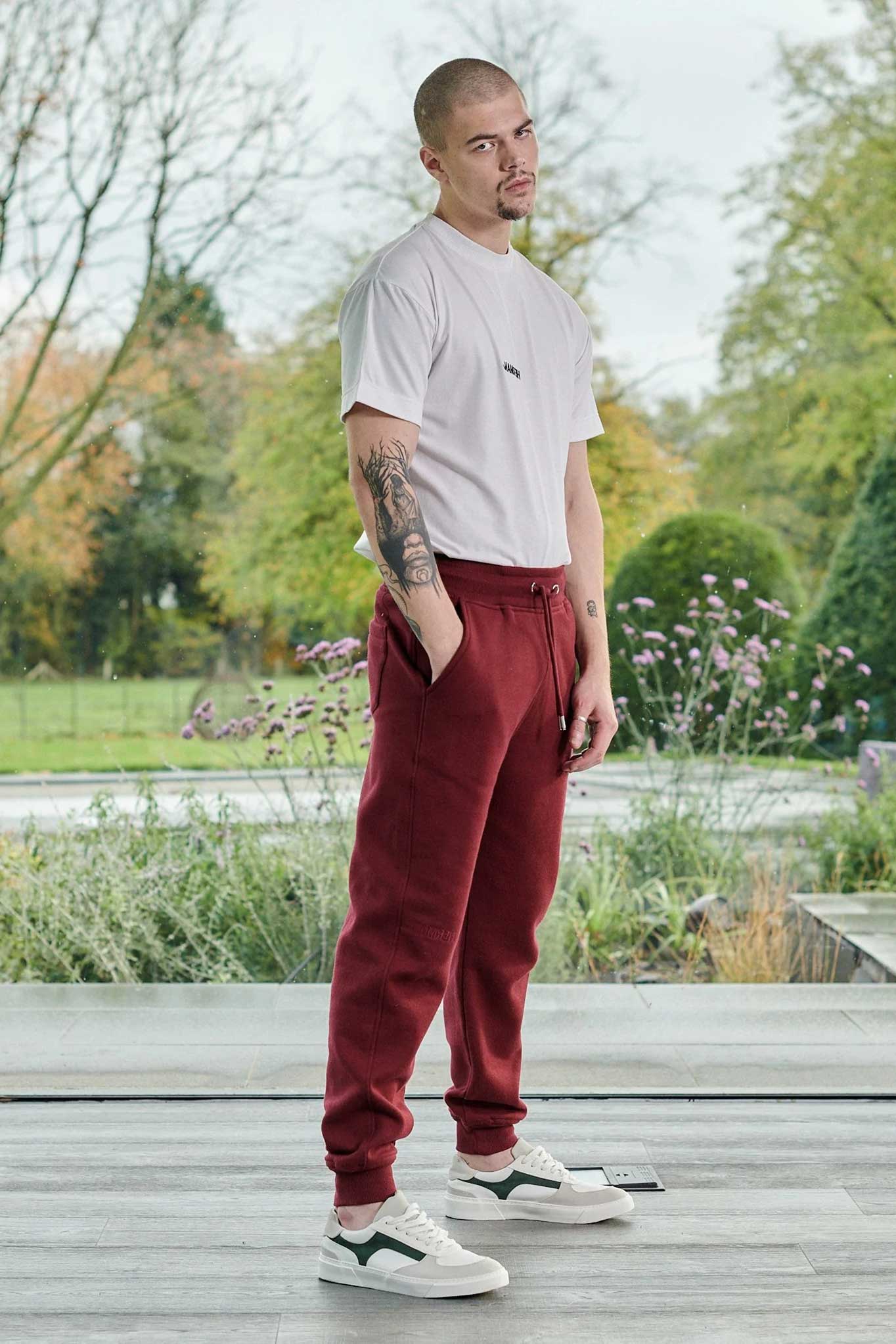 A model styled in the men's dark red tapered joggers with a white t-shirt.