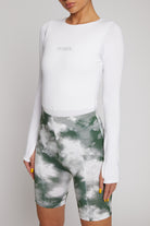 Close-up of the tonal embroidered logo on the white long-sleeve bodysuit.