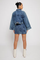 Back view of a model in the wide arm acid wash denim jacket and skirt.
