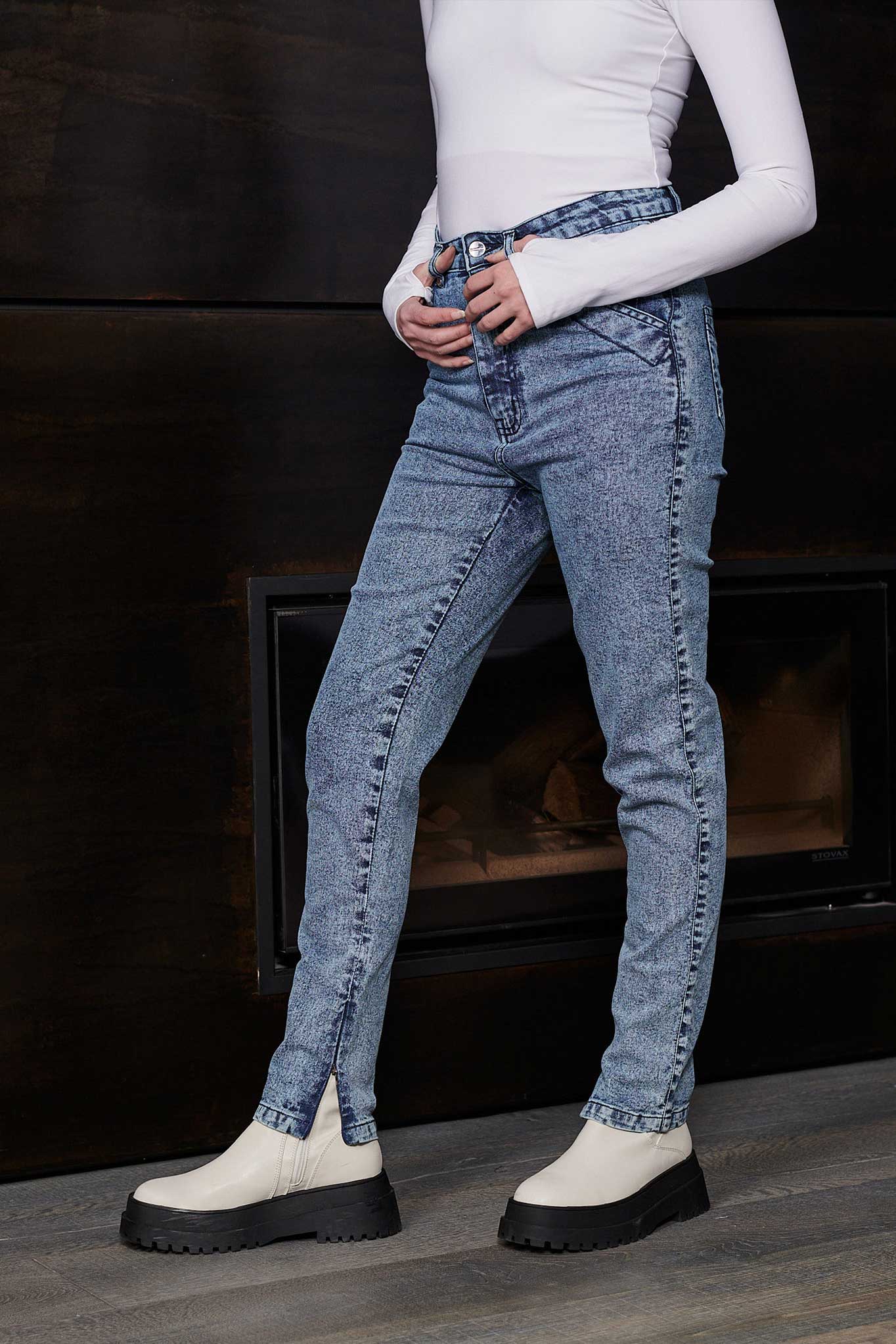 Side view of a model wearing women's blue acid wash jeans with an ankle zip